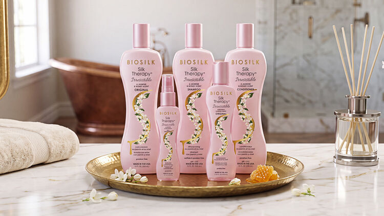 Five pink Biosilk Silk Therapy Irresistible bottles on a gold tray with jasmine blossoms and honeycomb.