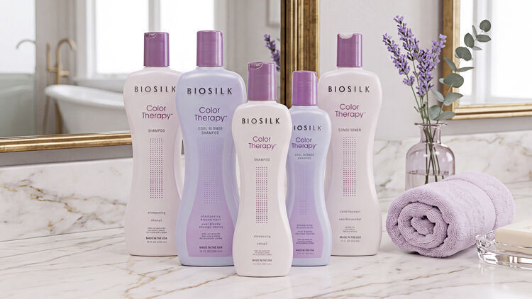 Five Biosilk Color Therapy bottles in blush and lavender on a marble vanity with a towel and dried lavender sprigs.