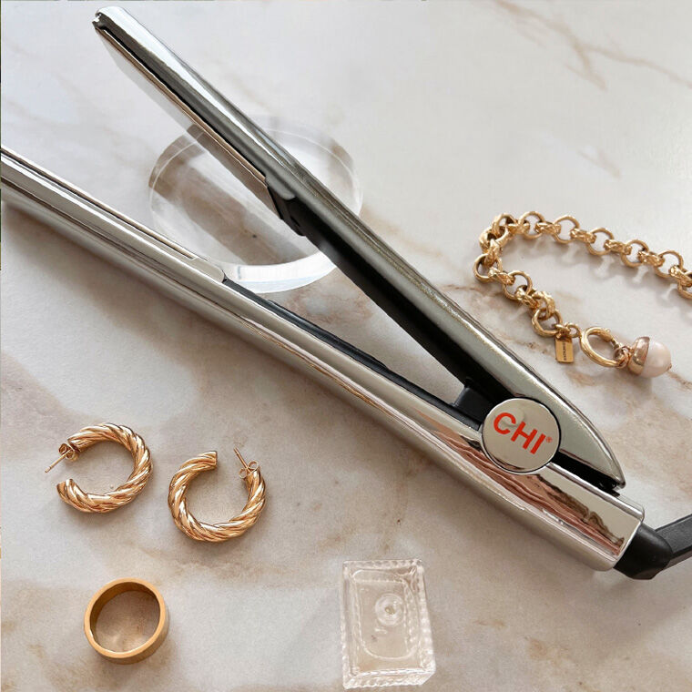 Sliver styling iron on a marble countertop surrounded by gold jewelry