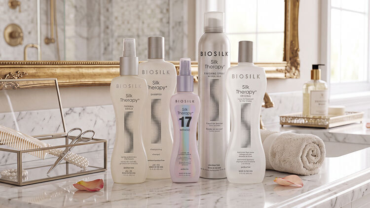 Five Biosilk Silk Therapy products, including shampoo, sprays, and 17 Miracle leave-in, on a marble bathroom counter.